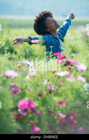 Eine Frau unter den Blumen mit ihren ausgestreckten Armen.  Kosmos von rosa und weißen Blüten. Stockfoto