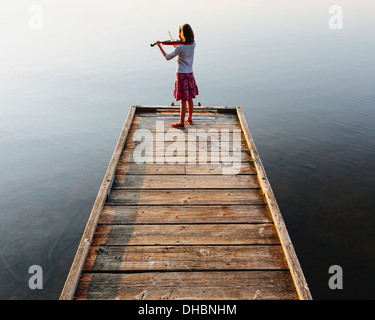 Ein zehn Jahre altes Mädchen, das Geigenspiel im Morgengrauen auf einem hölzernen Dock. Stockfoto