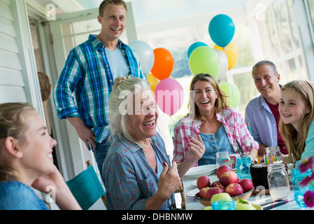 Eine Geburtstagsfeier in einer Landhausküche. Eine Gruppe von Erwachsenen und Kinder versammelten sich um einen Schokoladenkuchen. Stockfoto