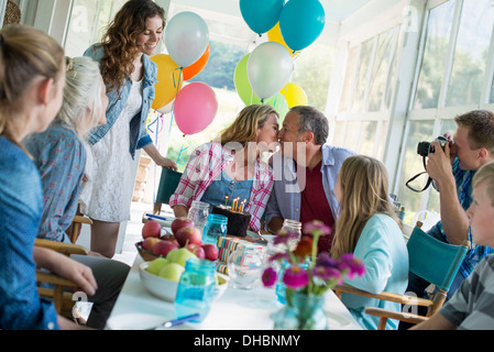 Eine Geburtstagsfeier in einer Landhausküche. Eine Gruppe von Erwachsenen und Kinder versammelten sich um einen Schokoladenkuchen. Stockfoto