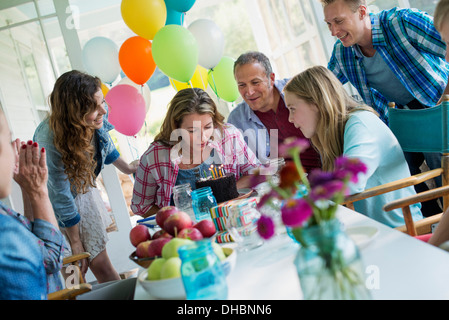 Eine Geburtstagsfeier in einer Landhausküche. Eine Gruppe von Erwachsenen und Kinder versammelten sich um einen Schokoladenkuchen. Stockfoto