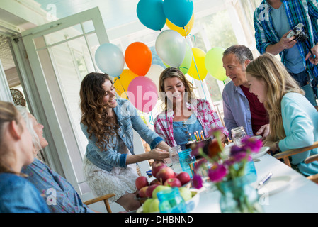 Eine Geburtstagsfeier in einer Landhausküche. Eine Gruppe von Erwachsenen und Kinder versammelten sich um einen Schokoladenkuchen. Stockfoto