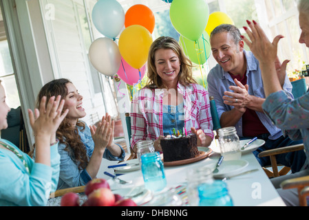 Eine Geburtstagsfeier in einer Landhausküche. Eine Gruppe von Erwachsenen und Kinder versammelten sich um einen Schokoladenkuchen. Stockfoto