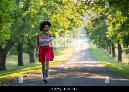 Eine Frau, die einen von Bäumen gesäumten Pfad hinunter. Stockfoto