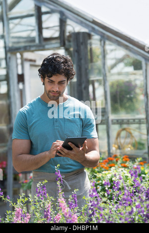 Ein junger Mann arbeitet in einer Gärtnerei, umgeben von blühenden Pflanzen. Stockfoto