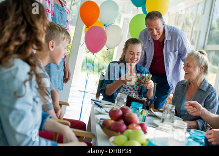 Eine Geburtstagsfeier in einer Landhausküche. Eine Gruppe von Erwachsenen und Kinder versammelten sich um einen Schokoladenkuchen. Stockfoto