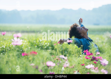 Eine Frau unter den Blumen mit ihren ausgestreckten Armen.  Kosmos von rosa und weißen Blüten. Stockfoto