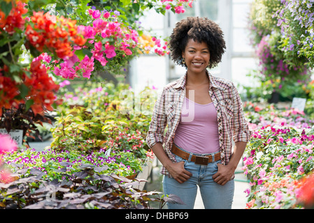 Eine Frau in einer Gärtnerei, umgeben von blühenden Pflanzen und Laub. Stockfoto