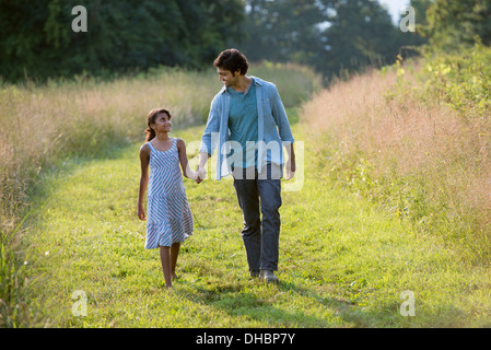 Ein Mann und ein junges Mädchen zu Fuß auf einem gemähten Weg das lange Gras, Hand in Hand. Stockfoto