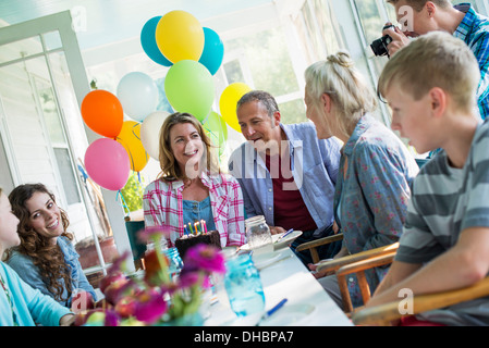 Eine Geburtstagsfeier in einer Landhausküche. Eine Gruppe von Erwachsenen und Kinder versammelten sich um einen Schokoladenkuchen. Stockfoto