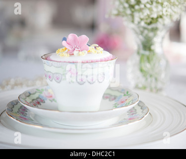 Eine florale China Tasse, Untertasse und Teller, mit vereisten Cupcake und Vase mit weißen Blumen Stockfoto