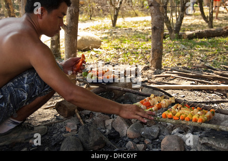 Horizontale Porträt von einem lokalen Lao Mann Barbecing Kebab in der Landschaft an einem sonnigen Tag. Stockfoto