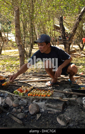 Vertikale Porträt von einem lokalen Lao Mann Barbecing Kebab in der Landschaft an einem sonnigen Tag. Stockfoto