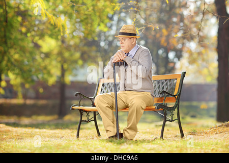 Trauriger senior Mann mit Stock sitzen auf einer Bank in einem Park an einem sonnigen Tag Stockfoto