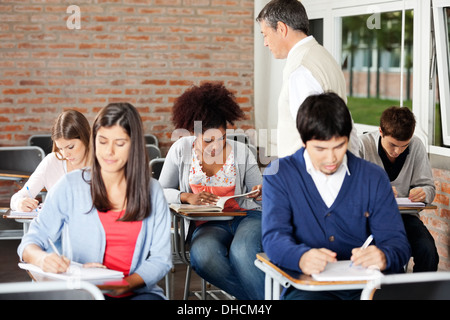 Studenten, die Prüfung zu schreiben, während Lehrer Aufsicht In Klasse Stockfoto