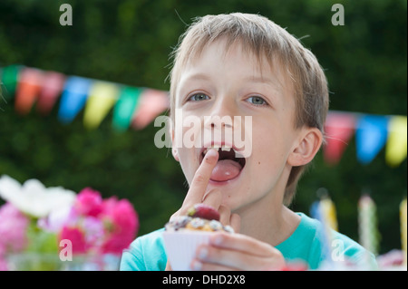 Fröhlicher Junge Essen Muffin auf einer Geburtstagsfeier Stockfoto