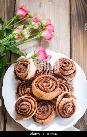 Zimtschnecken und rosa Rosen auf einem hölzernen Hintergrund Stockfoto