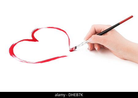 Zarte Frauenhand zieht eine rotes Herz-Form mit einem Pinsel auf einem weißen Hintergrund. Stockfoto