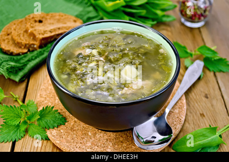 Suppe von Ampfer, Brennnessel und Spinat in eine Schüssel, Löffel, Brot, grüne Pfeffer gegen ein Holzbrett Stockfoto