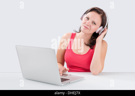 Junge Frau anhören von Musik über Bluetooth-Kopfhörer von Laptop und schaut in die Kamera Stockfoto