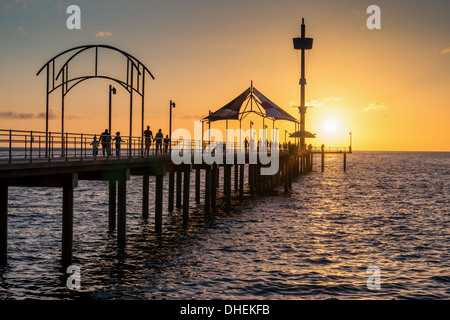 Menschen schlendern bei Sonnenuntergang am wunderschönen Brighton Pier in Australien, einem Meer mit kristallklarem Wasser und einem unberührten Sandstrand Stockfoto