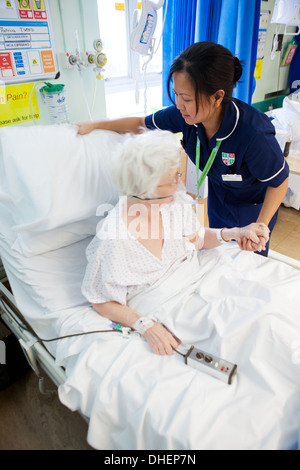 Eine philippinische Krankenschwester hilft eine ältere Frau im Bett UK Stockfoto