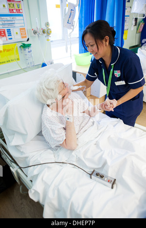 Eine philippinische Krankenschwester hilft eine ältere Frau im Bett UK Stockfoto