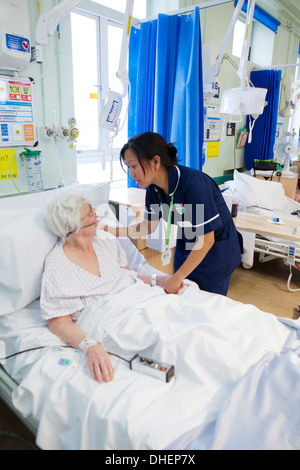 Eine philippinische Krankenschwester hilft eine ältere Frau im Bett UK Stockfoto