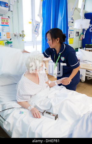 Eine philippinische Krankenschwester hilft eine ältere Frau im Bett UK Stockfoto