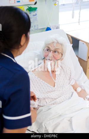 Eine philippinische Krankenschwester hilft eine ältere Frau im Bett UK Stockfoto