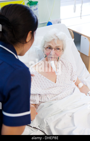 Eine philippinische Krankenschwester hilft eine ältere Frau im Bett UK Stockfoto