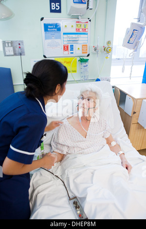 Eine philippinische Krankenschwester hilft eine ältere Frau im Bett UK Stockfoto