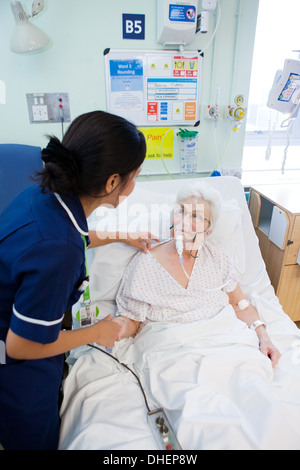 Eine philippinische Krankenschwester hilft eine ältere Frau im Bett UK Stockfoto