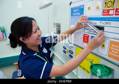 Eine philippinische Krankenschwester ändert sich die Patienten Details über ein Bett von NHS UK Stockfoto