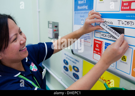 Eine philippinische Krankenschwester ändert sich die Patienten Details über ein Bett von NHS UK Stockfoto