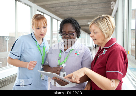Drei Krankenschwestern verwenden Sie ein iPad zu einem Patienten zu suchen Hinweise GROSSBRITANNIEN Stockfoto