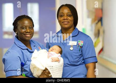 Eine Hebamme hält ein neugeborenes Baby, während ein Kollege in einem Krankenhausflur UK steht Stockfoto