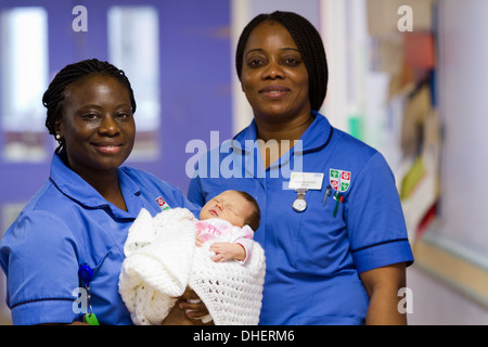 Eine Hebamme hält ein neugeborenes Baby, während ein Kollege in einem Krankenhausflur UK steht Stockfoto