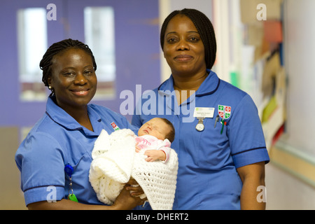 Eine Hebamme hält ein neugeborenes Baby, während ein Kollege in einem Krankenhausflur UK steht Stockfoto