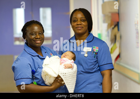 Eine Hebamme hält ein neugeborenes Baby, während ein Kollege in einem Krankenhausflur UK steht Stockfoto