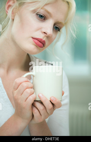 Wehmütig aussehende junge Frau mit einem Kaffee Stockfoto