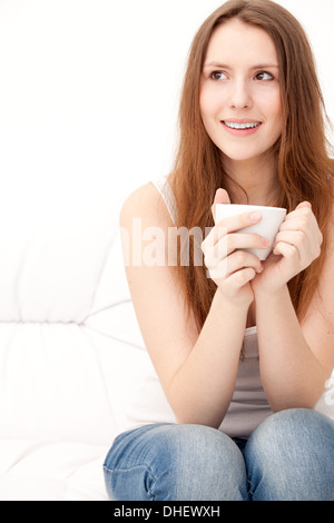 Faszinierende Frau hält eine Tasse auf einem Sofa sitzt Stockfoto