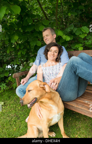 Älteres Paar sitzt auf der Gartenbank mit Hund Stockfoto