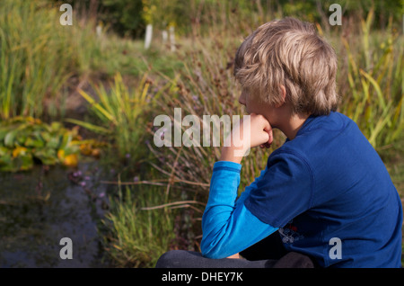 Nachdenklichen jungen beobachten und warten neben einem Teich im Spätsommer / Anfang Herbst. Stockfoto