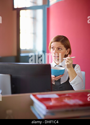 Büroangestellte, Frühstücks-Cerealien am Schreibtisch zu essen Stockfoto