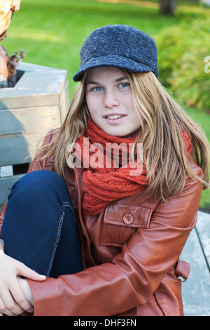 Junges Mädchen im Freien auf einer Bank sitzen. Sie trägt eine Hut und Leder Jacke. Stockfoto