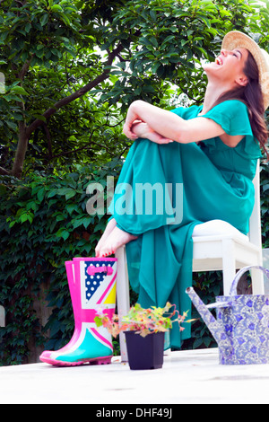 Junge Frau trägt grünes Kleid sitzen auf Stuhl vor Lachen Stockfoto