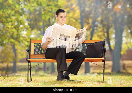 Geschäftsmann, sitzen auf einer Bank und liest eine Zeitung in einem park Stockfoto