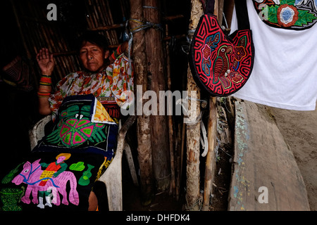 Eine Frau aus dem Guna Menschen zeigt eine Auswahl an traditionellen handgemachten Molas zum Verkauf an ihrem Haus in Carti Sugtupu Island Village durch Guna Eingeborenen als Kuna in der "Comarca" (Region) der Guna Yala im Archipel von San Blas Blas Inseln im Nordosten von Panama mit Blick auf das Karibische Meer bekannt gegeben. Stockfoto