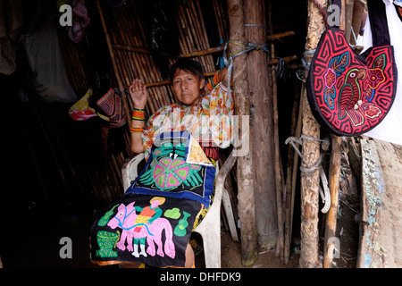 Eine Frau aus dem Guna Menschen zeigt eine Auswahl an traditionellen handgemachten Molas zum Verkauf an ihrem Haus in Carti Sugtupu Island Village durch Guna Eingeborenen als Kuna in der "Comarca" (Region) der Guna Yala im Archipel von San Blas Blas Inseln im Nordosten von Panama mit Blick auf das Karibische Meer bekannt gegeben. Stockfoto